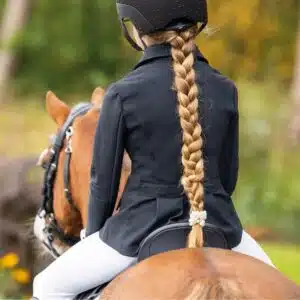 Jeune cavalière portant la veste de concours Amilara QHP à cheval vue de dos d'une jeune cavalière portant la veste de concours Amilara QHP à cheval