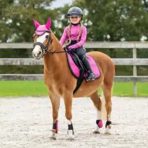 Tapis de selle Isalyn QHP rose satiné porté par un poney sellé monté par une jeune cavalière