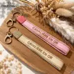 Porte-clés Cavalière en Or EQUESTRIAN SHOP – Rose et beige Porte-clés Cavalière en Or EQUESTRIAN SHOP en tissu brodé, présentés en rose et beige avec des détails dorés