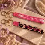 Porte-clés Pétasse à Cheval EQUESTRIAN SHOP – Léopard et rose Porte-clés Pétasse à Cheval EQUESTRIAN SHOP présentés en coloris léopard et rose avec inscription brodée et attaches dorées